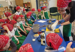 Dziewczynka przesiewa mąkę, nauczycielka odmierza mąkę w szklance
