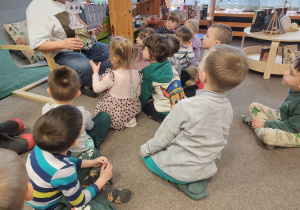 Dzieci siedzą na dywanie, obserwują pokazywaną przez bibliotekarkę sylwetkę kota
