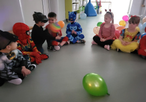 Dzieci siedzą w kole i podają sobie balona
