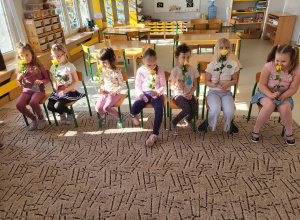 Dziewczynki siedzą w rzędzie na krzesłach z upominkami w rękach