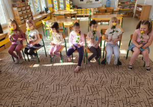 Dziewczynki siedzą w rzędzie na krzesłach z upominkami w rękach