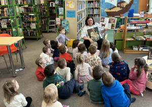 Pani bibliotekarka pokazuje dzieciom w książeczce zdjęcia różnych ras kotów
