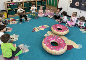 Dzieci zwijają sznurek na rurkę, przyciągając do siebie balony w kształcie donutów