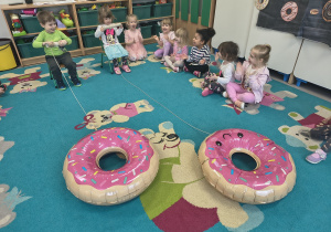 Dzieci zwijają sznurek na rurkę, przyciągając do siebie balony w kształcie donutów