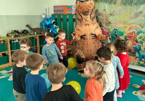 Dzieci tańczą w kole z wielkim dmuchanym dinozaurem