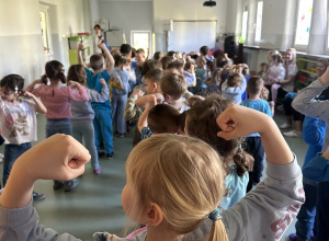 Dziewczynka na tle innych dzieci pokazuje gest ,,bycia silnym''