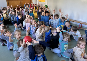 Dzieci siedzą w rzędach i przekazują sobie piłki