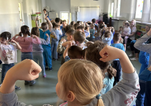 Dziewczynka na tle innych dzieci pokazuje gest ,,bycia silnym''
