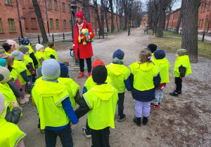 Dzieci słuchają przewodniczki, w tle kamienice