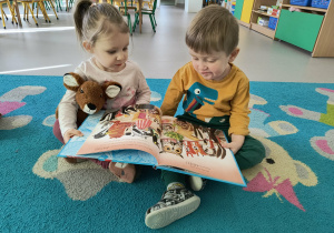 Dziewczynka i chłopiec siedzą na dywanie wspólnie oglądając ilustracje w książce