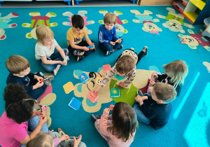 Dzieci siedzą w kole. Chłopiec dopasowuje zakładkę do odpowiedniej okładki książki